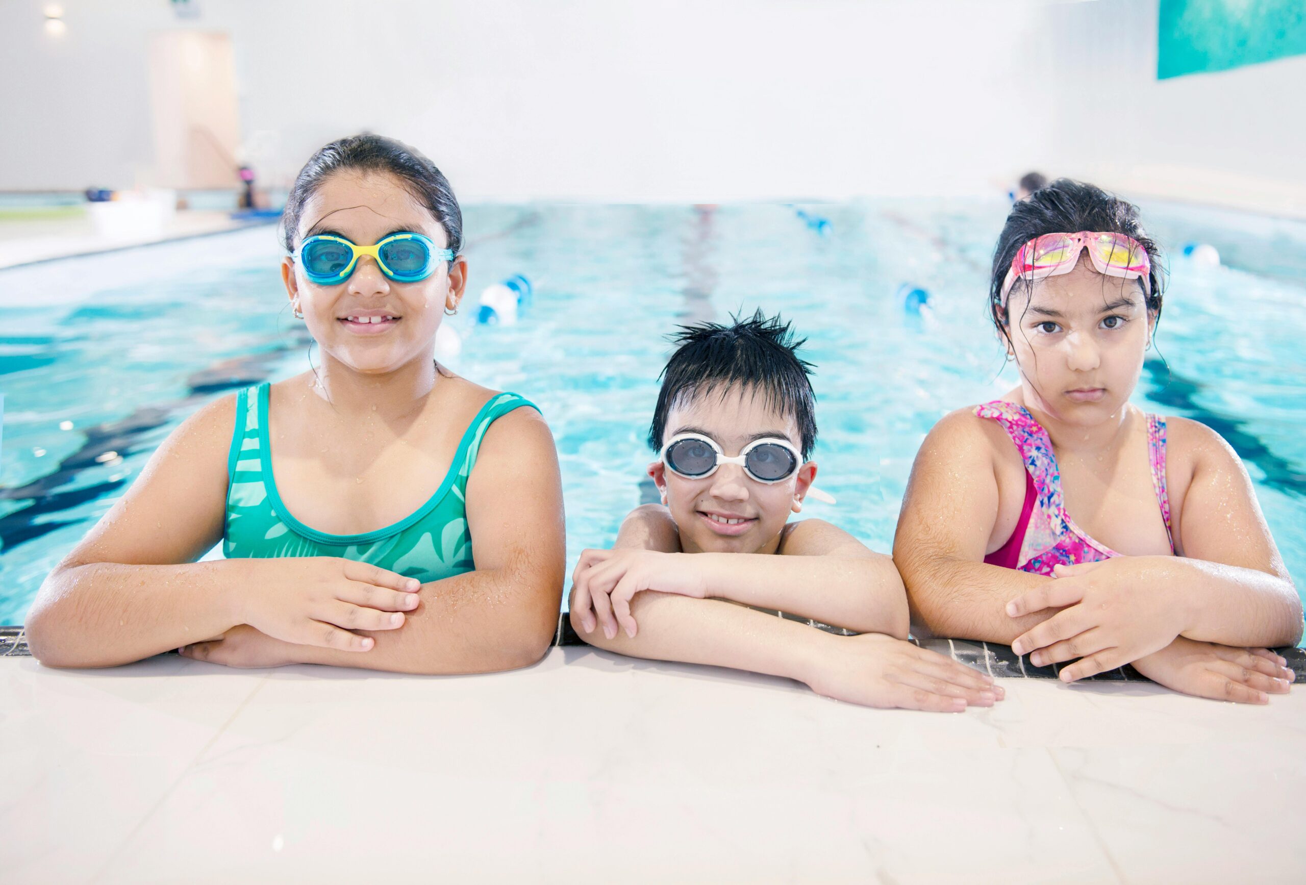 Three kids pose for a picture while swimming in a pool facility.